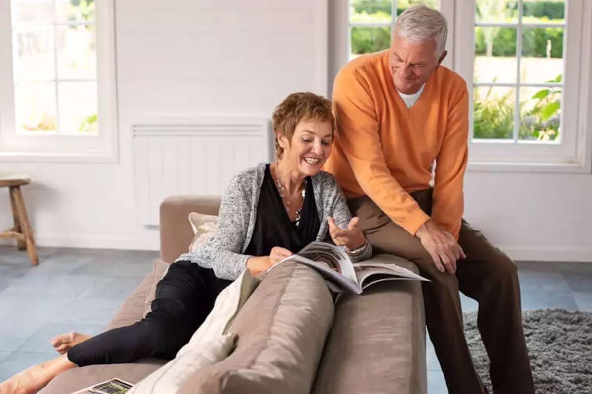 Couple dans un fauteuil feuilletant un magazine avec un radiateur de chauffage électrique sur le mur à côté d'eux
